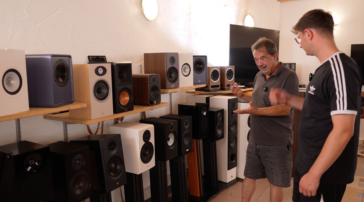Martin, Gründer von MD Sound, erklärt Daniel vor einer Wand voller Regallautsprecher im Vorführraum